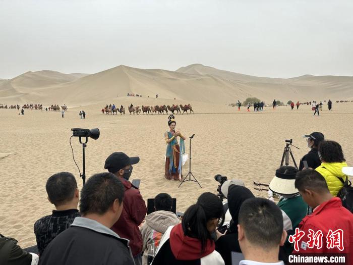 圖為2023年4月底，敦煌大漠“逐舞者”奧楠在鳴沙山月牙泉景區(qū)視頻直播，吸引游人圍觀?！●T志軍 攝